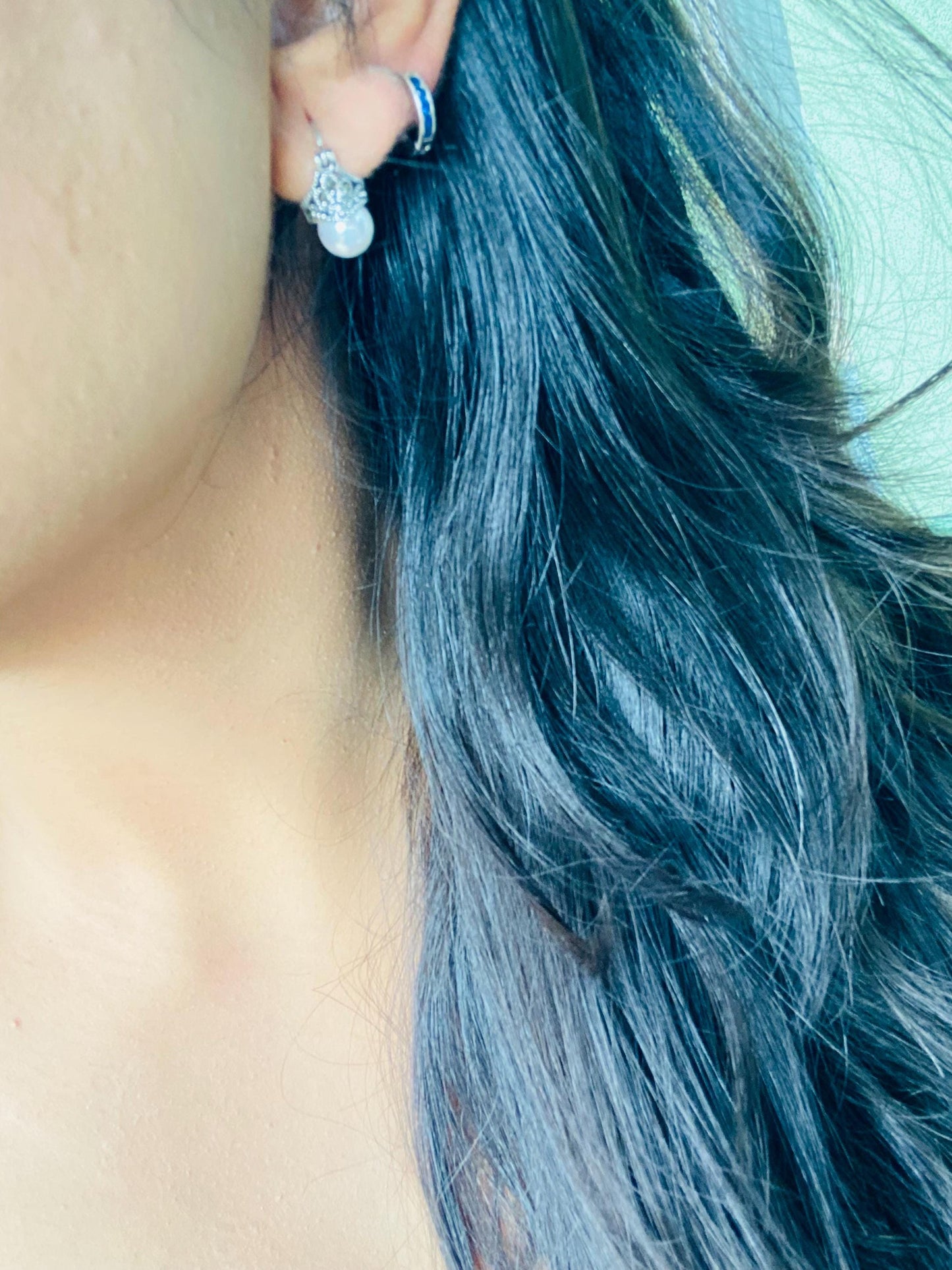 Close-up of a person's ear with blue hair and earrings.