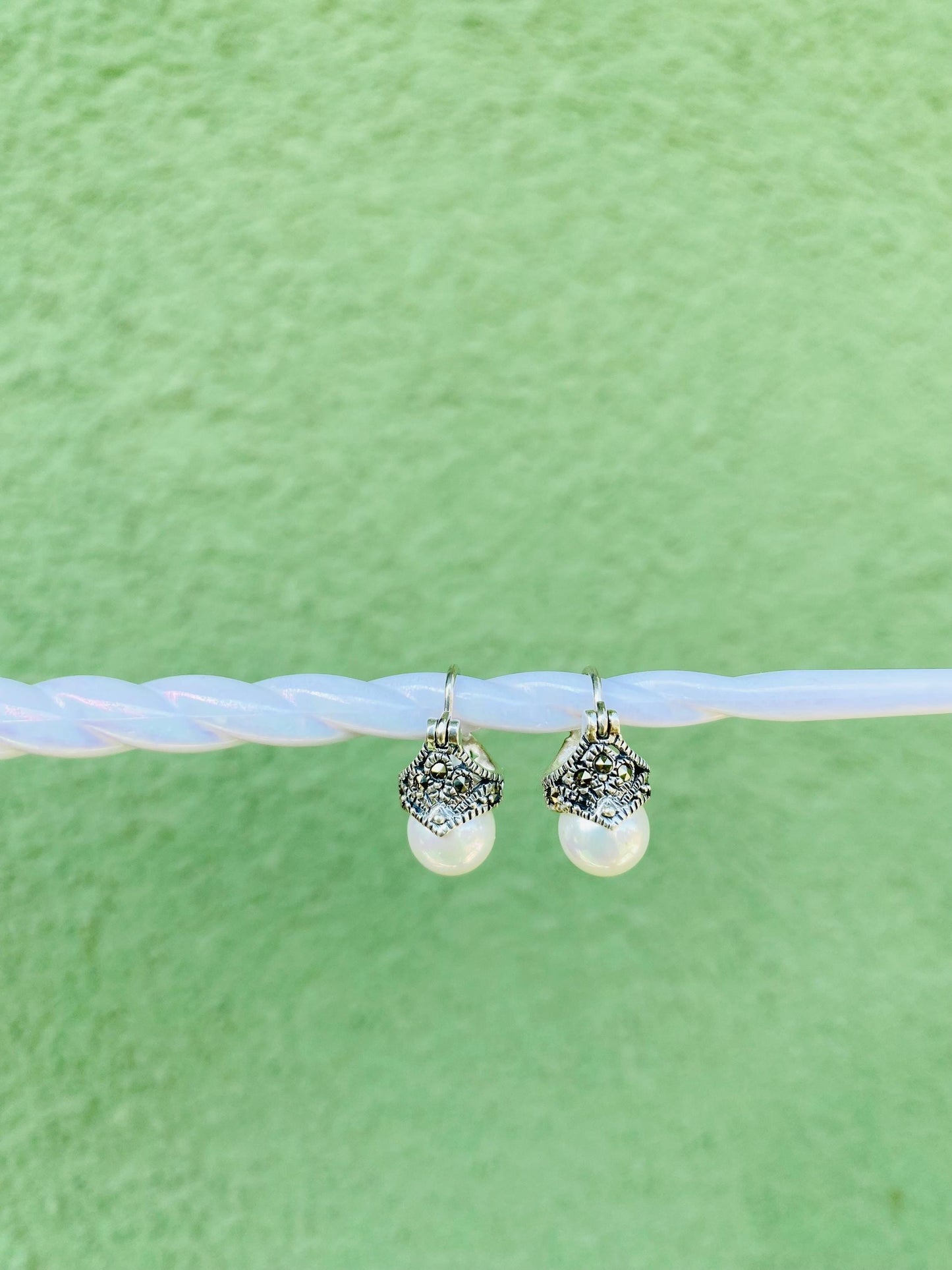 Pearl earrings with silver tops on a light blue string against a green background