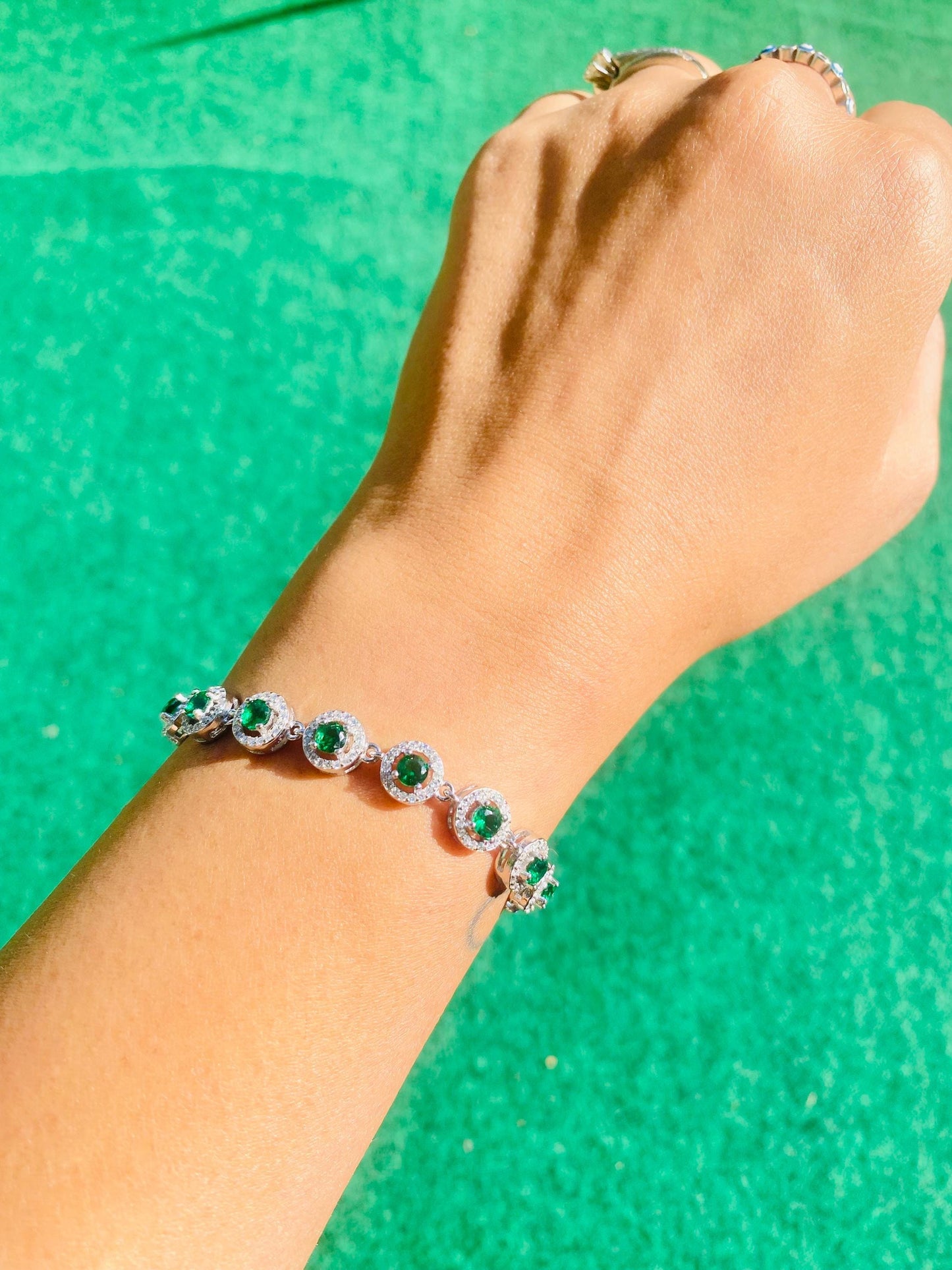 Hand wearing a bracelet with green gemstones against a green background