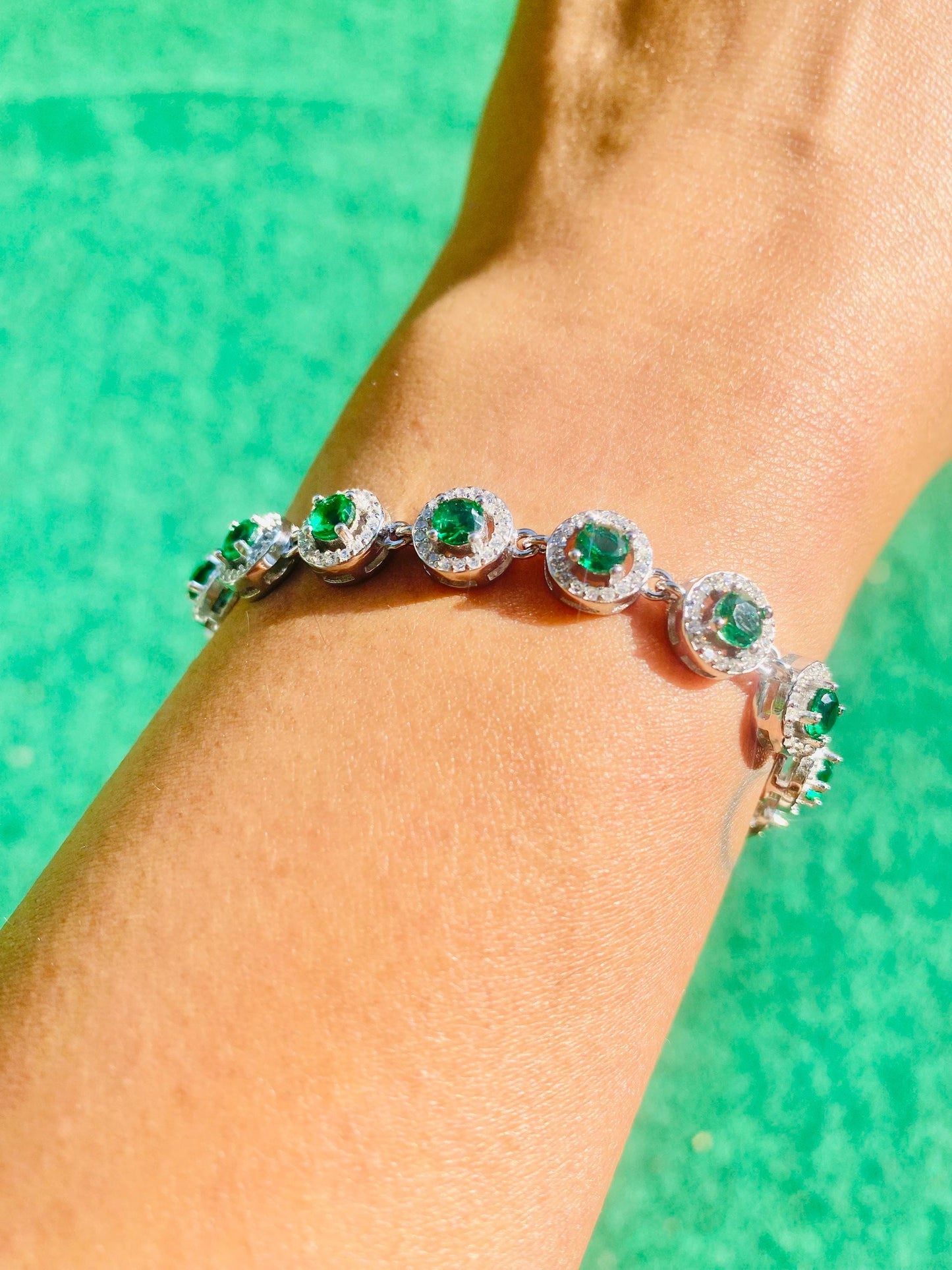 Silver bracelet with green gemstones on a person's wrist against a green background