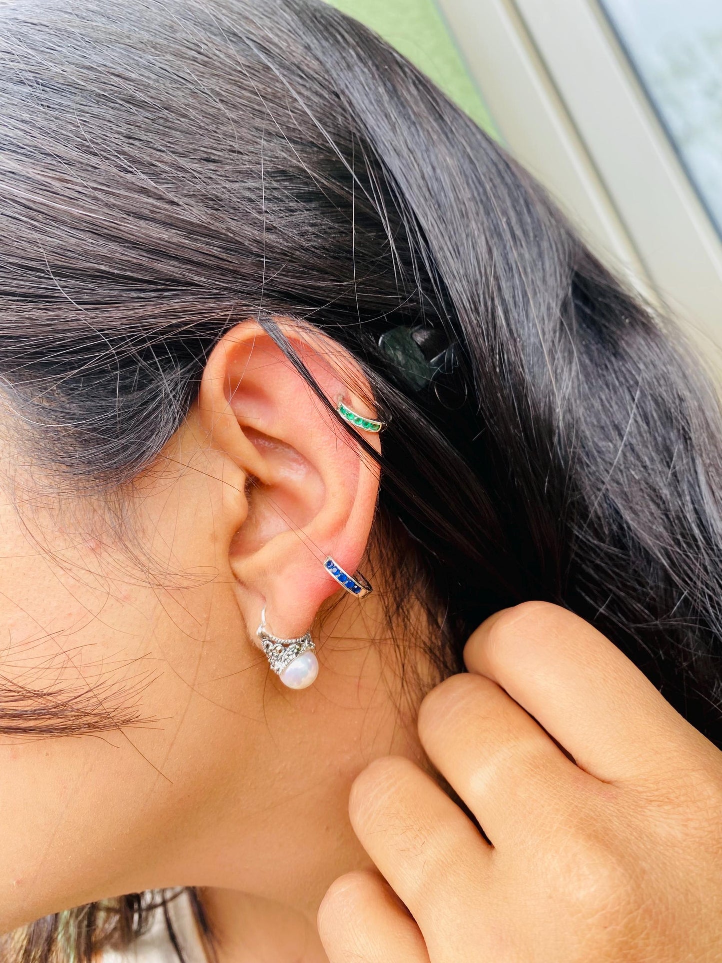 Close-up of an ear with earrings and a hand adjusting hair.
