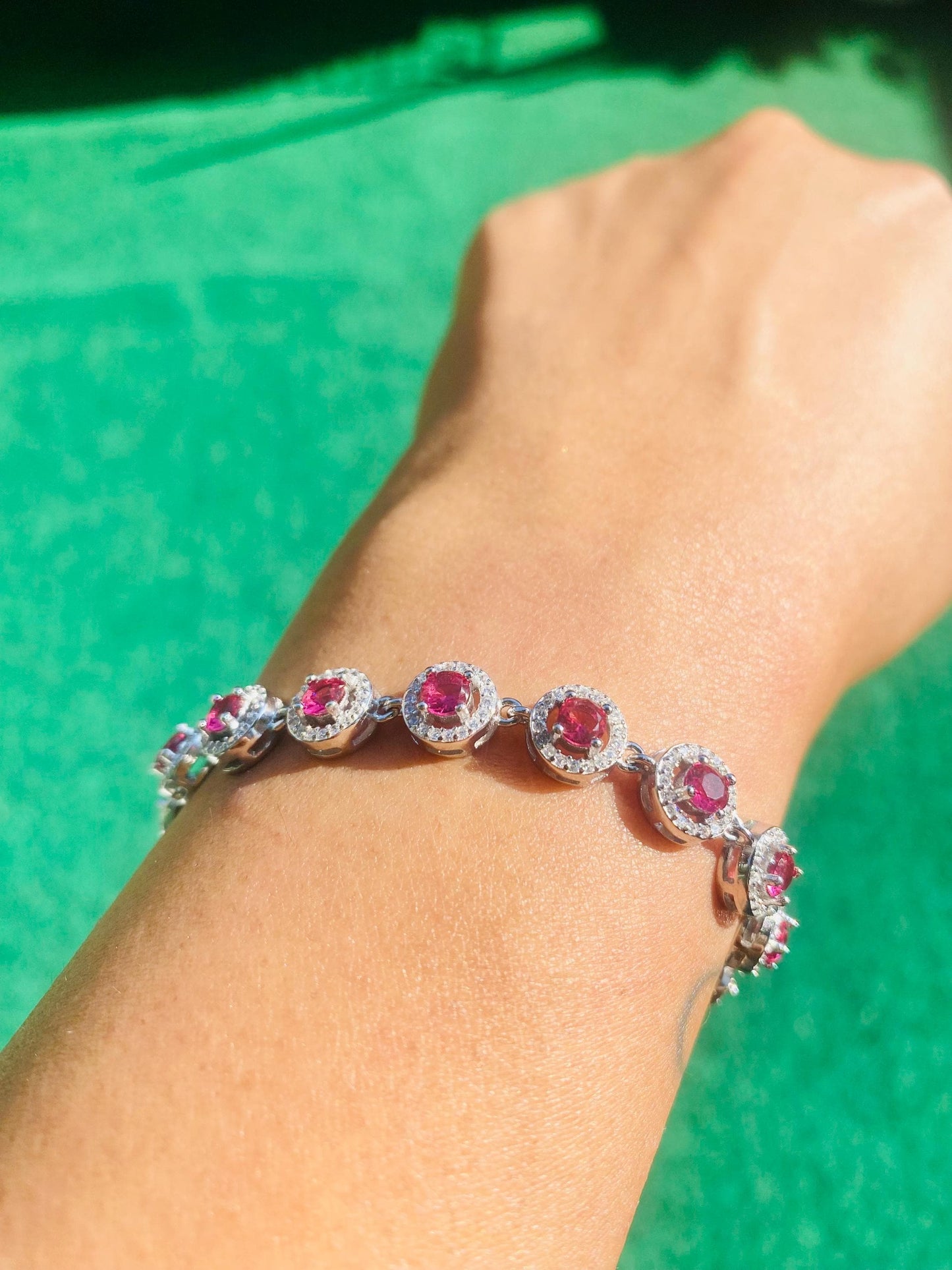 Silver bracelet with pink gemstones on a wrist against a green background