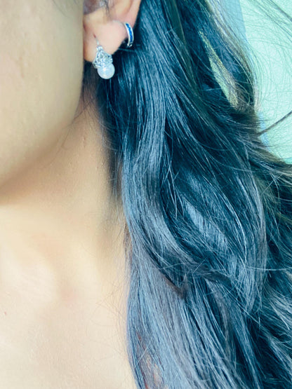 Close-up of a person's ear with blue hair and earrings.