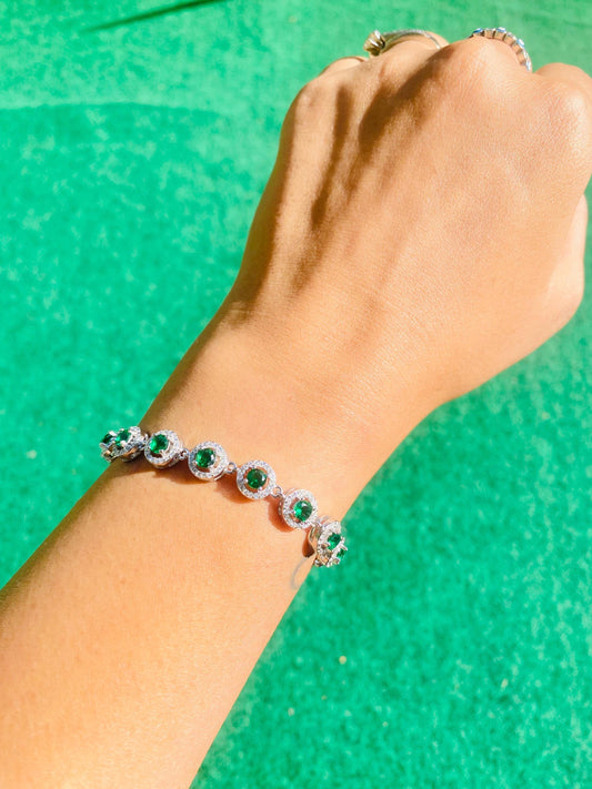 Hand wearing a bracelet with green gemstones against a green background
