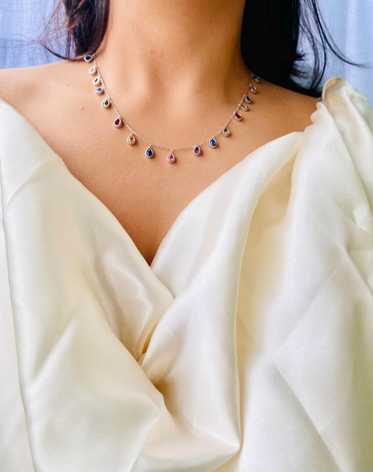 Necklace with multicolored gemstones worn by a person in a white garment.